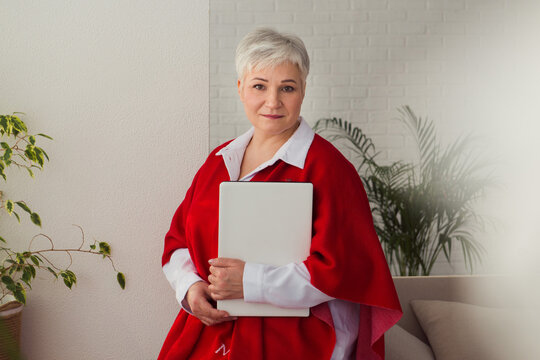 gray-haired woman white shirt standing at workplace with laptop and planner