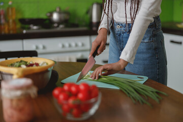 Female hands holding knife cutting fresh spring onion on silicone board indoor in kitchen