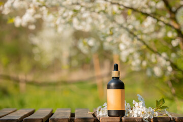 Cosmetic bottle on wooden table in blooming tree spring garden