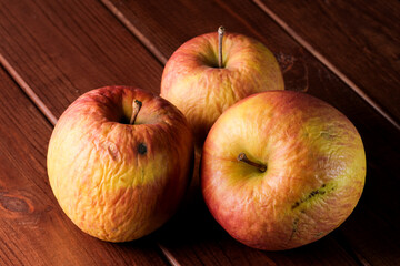 Spoiled shriveled rotten apples on a dark wooden background close-up