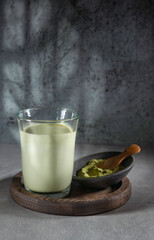 A glass of Matcha latte tea with Matcha powder in a bowl and a glass jar on a gray background