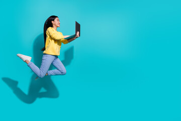 Full length photo of pretty funny lady dressed yellow sweater jumping working device empty space isolated turquoise color background