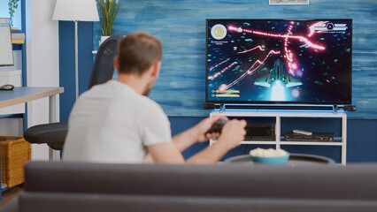Man holding controller playing action space shooter on console disappointed because losing online...