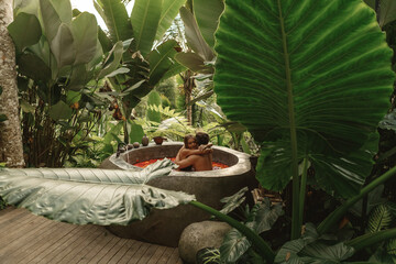 Young couple relaxing at spa, enjoy honeymoon on Bali island, taking bath full of flowe petals in the jungle. Beautiful couple resting in hotel spa