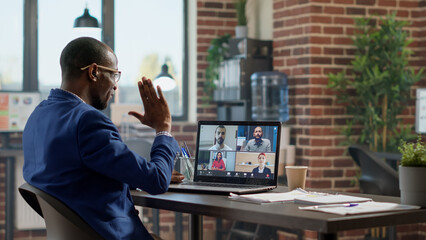 Young businessman attending teleconference meeting on laptop, talking to colleagues on online...