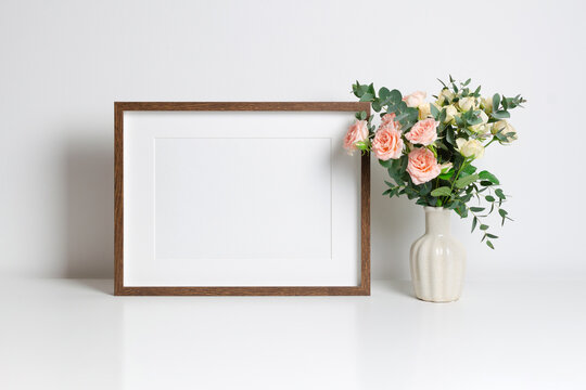 Wooden frame mockup in white interior with copy space for artwork and fresh roses bouquet