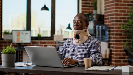 Financial analyst with physical injury wearing medical neck collar at office job, using cervical...