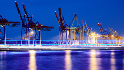 Terminal Burchardkai in City of Hamburg during night time with blue colored light stripes from a tourism boat on the river Elbe. Long exposure shot.