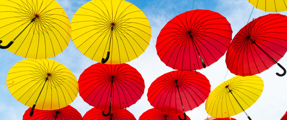 Fototapeta na wymiar Red and yellow umbrellas hanging sky background bottom-up