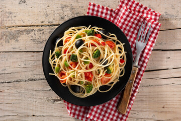 Spaghetti with vegetables(broccoli,tomatoes,peppers) on wooden table. Top view