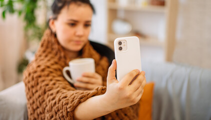Close-up of a woman holding a mug of tea in her hand, and talking on a video call with her doctor. A woman who is not feeling well calls a doctor from home via the Internet. selective focus