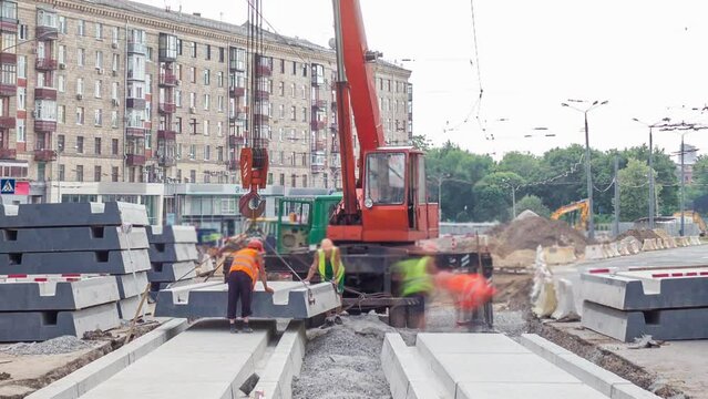 Installing concrete plates by crane at road construction site panoramic timelapse. Industrial workers with hardhats and uniform. Reconstruction of tram tracks in the city street