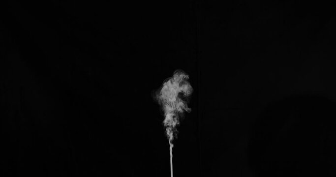 Slow motion single stream of smoke erupting from the bottom middle of frame that slowly drifts rightwards. Shot on black for easy composting.