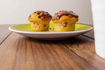 Two chocolate chip muffins on a yellow plate and wooden table . Copy space. Premium quality bakery product.