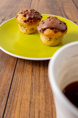 Two chocolate chip muffins on a yellow plate and white cup of tea and wooden table . Copy space. Premium quality bakery product.