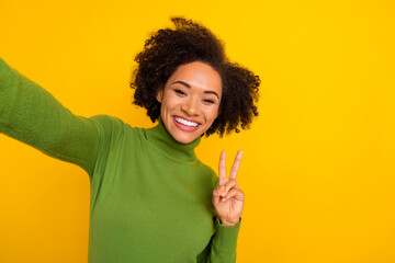 Photo of young lovely lady show fingers peace hello v-symbol make selfie isolated over yellow color background