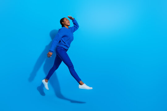 Photo of excited dreamy lady dressed pullover jumping looking far away empty space isolated blue color background