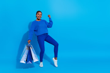 Photo of lucky charming lady dressed pullover walking shopping rising fist empty space isolated...