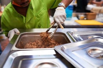 A chef assistant gets a portion of pulled beef with tongs