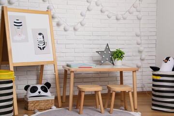 Stylish child room interior with wooden table and board near white brick wall