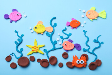Fototapeta na wymiar Colorful fish, water plants and stones made with play dough on light blue background, flat lay