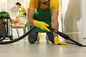 Professional janitor in uniform vacuuming floor indoors, closeup