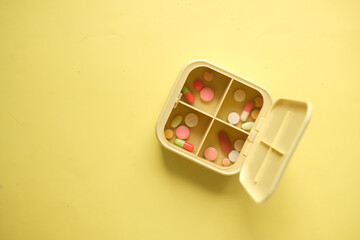 close up of medical pills in a pill box on yellow background 