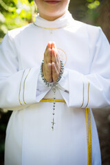 Dziecko przystępujące do sakramentu Pierwszej Komunii Świętej trzyma w ręku różaniec i modlitewnik - obrazy, fototapety, plakaty
