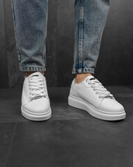 Close-up photo of men's white sneakers with jeans. White sneakers on his feet
