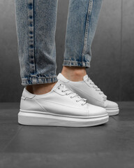 Close-up photo of men's white sneakers with jeans. White sneakers on his feet