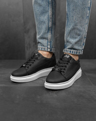 Close-up photo of men's black sneakers with jeans. White sneakers on his feet