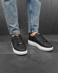 Close-up photo of men's black sneakers with jeans. White sneakers on his feet
