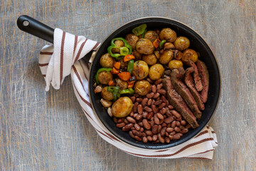 big fried steak with stewed new potatoes with vegetables and beans. Dinner dish in a frying pan
