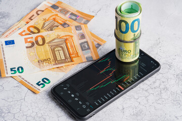 Euro banknotes and smartphone with currency exchange rate chart on screen. Investment in crypto