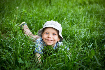 Chłopiec tarza się w trawie i śmieje w głos, dziecko turla się i leży na trawie z radością - obrazy, fototapety, plakaty
