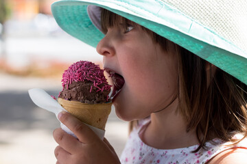 Mała dziewczynka w kapeluszu je lody truskawkowe, wakacyjna ochłoda, dzieci lubią lody - obrazy, fototapety, plakaty