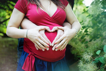Kobieta w ciąży, brzuszek ciążowy, rodzice robią serce z dłoni na brzuchu, czekając na dziecko, serduszko z rąk, goły brzuch - obrazy, fototapety, plakaty