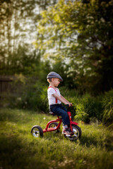 Chłopiec uczy się jeździć na rowerze trójkołowym w letnim słońcu - obrazy, fototapety, plakaty