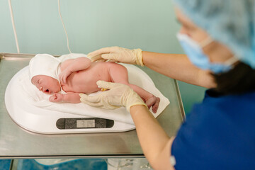 Nurse with newborn baby in postpartum ward. Medical staff caring, weighing a newborn baby on scales...