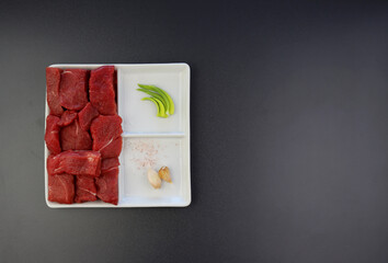 Pieces of fresh beef in a square plate on a gray background. Red meat.