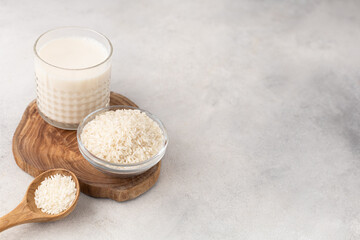Glass cup of rice milk with a bowl of rice on a light background