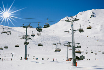 Many fully occupied ski lifts crossing a ski slope against blue sky