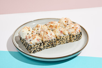 Baked Maki roll with bacon on ceramic plate. Hot sushi roll with sesame outside, bacon and cheese topped on coloured background. Japanese menu concept. Hot maki sushi in modern style.