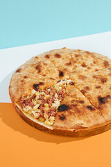 Closed pizza with minced meat, potatoes and cheese on coloured background. Meat pie with potatoes and cheese in minimal style. American pizza delivery concept with color backdrop.