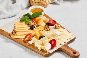 Cheese platter with nuts, honey sauce and olives on wood board. Cheeseboard on white concrete...