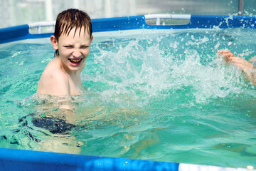 Happy boy splashing on summer pool having fun leisure activity