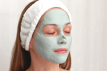 Woman with white band on head with blue dry clay mask on face with closed eyes over white background