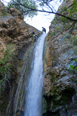 MAN DESCENDING A WATERFALL IN A FOREST