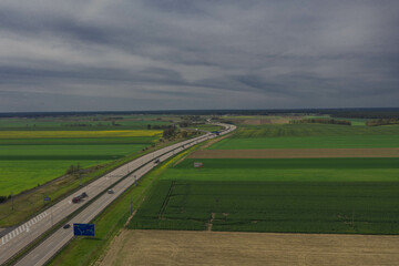 Słoneczny dzień. Niebo lekko zachmurzone, równina pokryta polami uprawnymi i łąkami. Na równinie jest betonowa, dwupasmowa droga. Widać jadące po niej samochody. © boguslavus