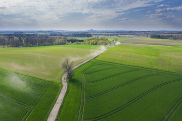 Równina pokryta łąkami i polami sfotografowana z drona.
Droga polna przebiegająca przez pola i łąki widziana z wysokości. Zdjęcie z drona. W oddali widać zabudowania pobliskiej wioski. - 502760502